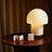 Table lamp on a round wooden table with a warm glow against a dark curtain background and rise 3-pack condoms. 2